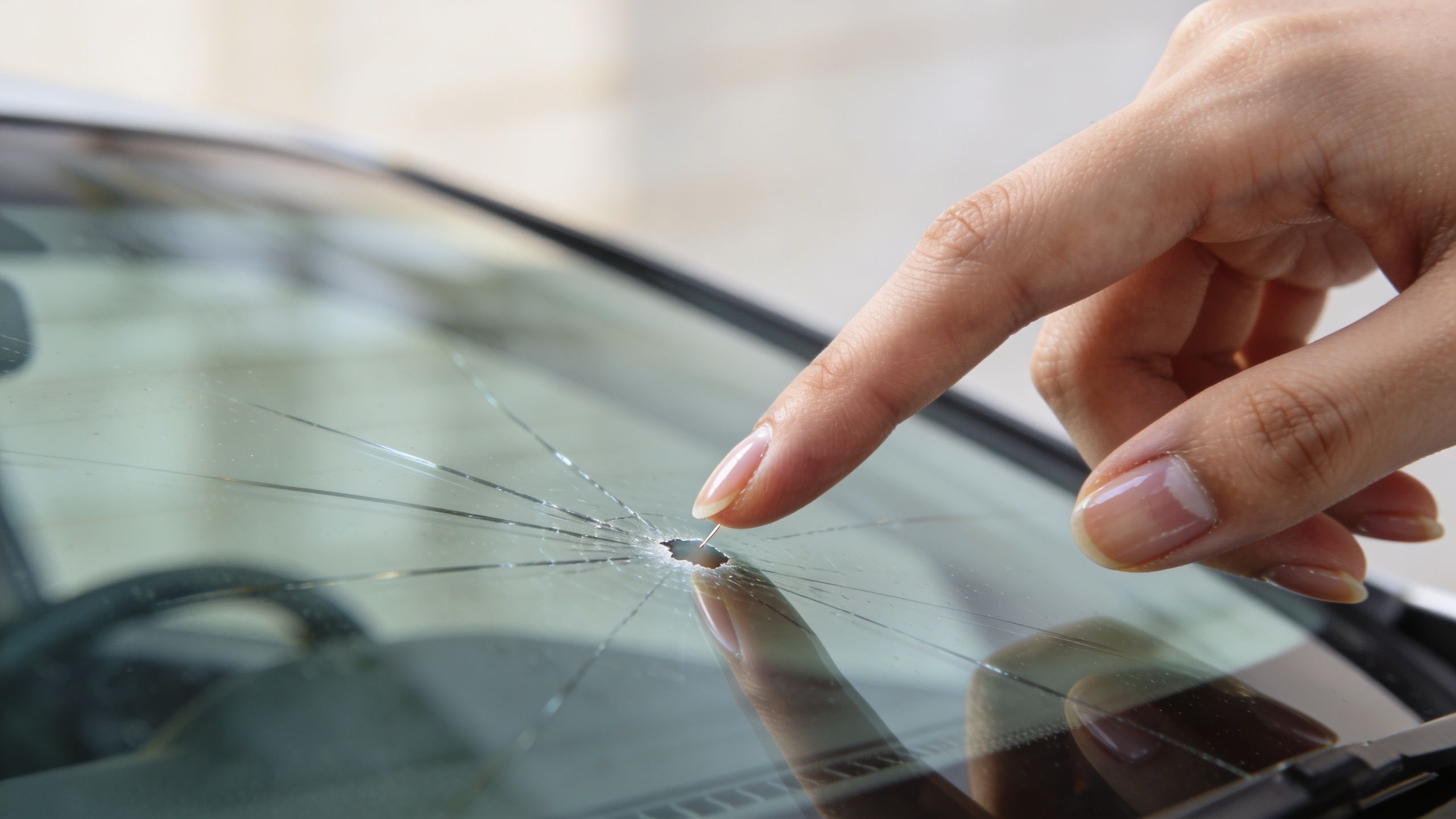 En person peger på en tydelig stjerneformet revne og et stenslag i en bilforrude med en finger.