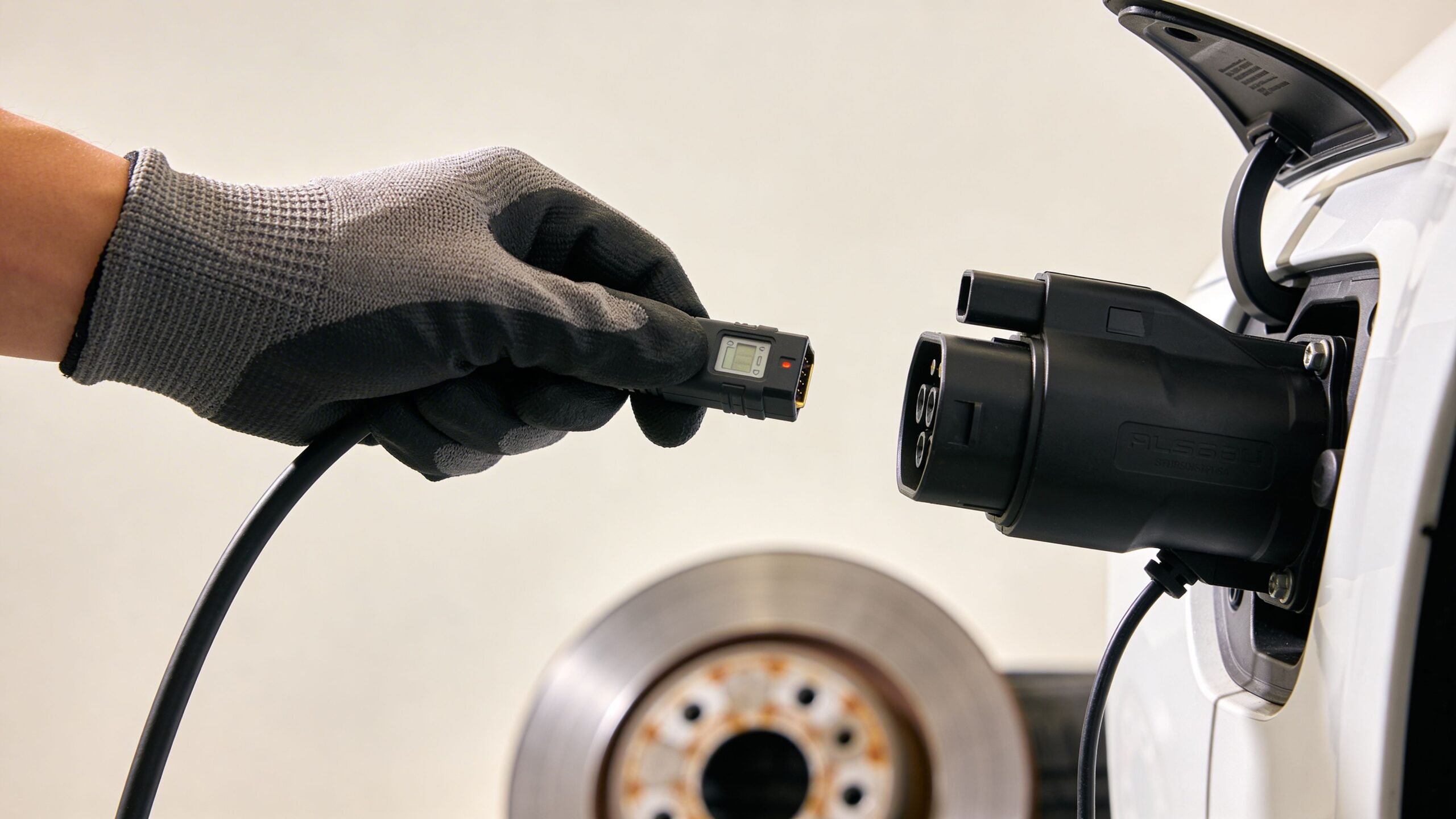 En mekaniker i arbejdshandsker forbereder sig på at tilslutte et ladekabel til en moderne elbil til reparation.