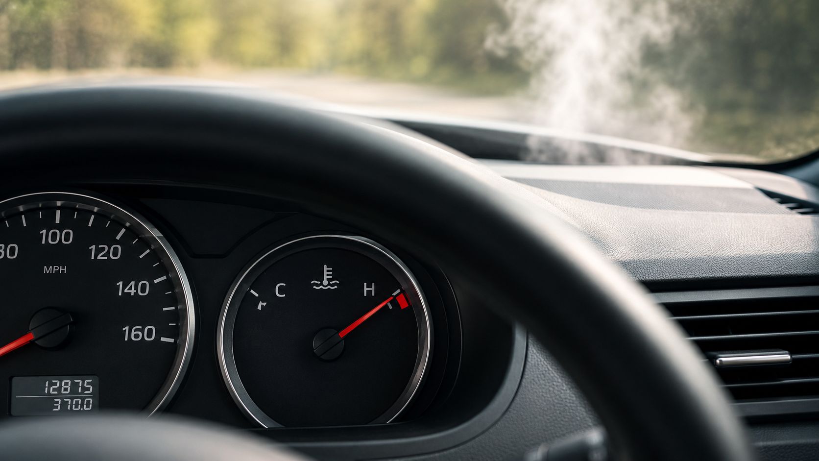 Bilens instrumentbræt viser en overophedet motor med damp, der stiger op fra kølerhjelmen under kørsel.